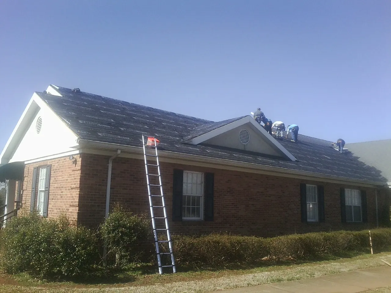 Crew tearing shingles off a brick ranch roof with a ladder set — Emergency Roof Repair work by our crew in Arendtsville