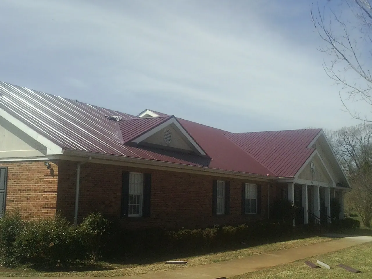 Red metal roof with gabled entries on a long brick building, from a Hail Damage Roof Repair job in Arendtsville