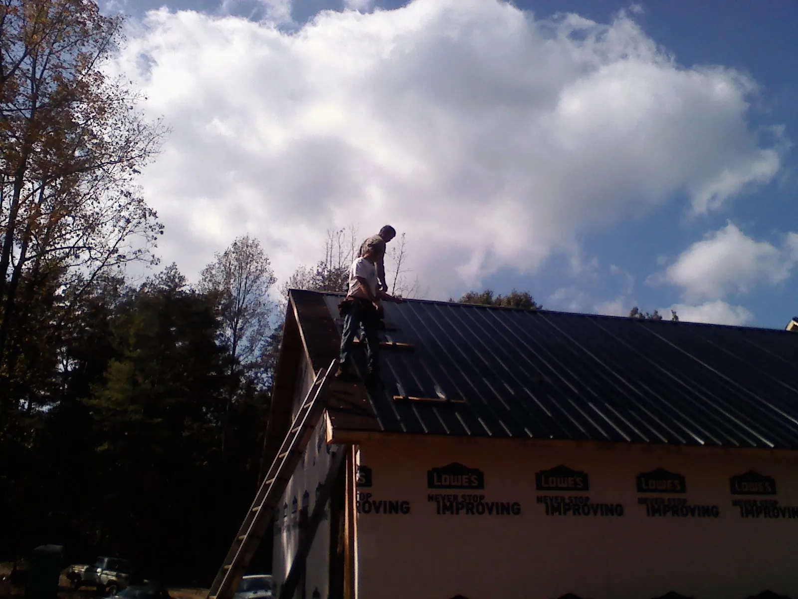 Roofer fastening dark metal panels high against a cloudy sky, from a Roof Inspection job in Arendtsville