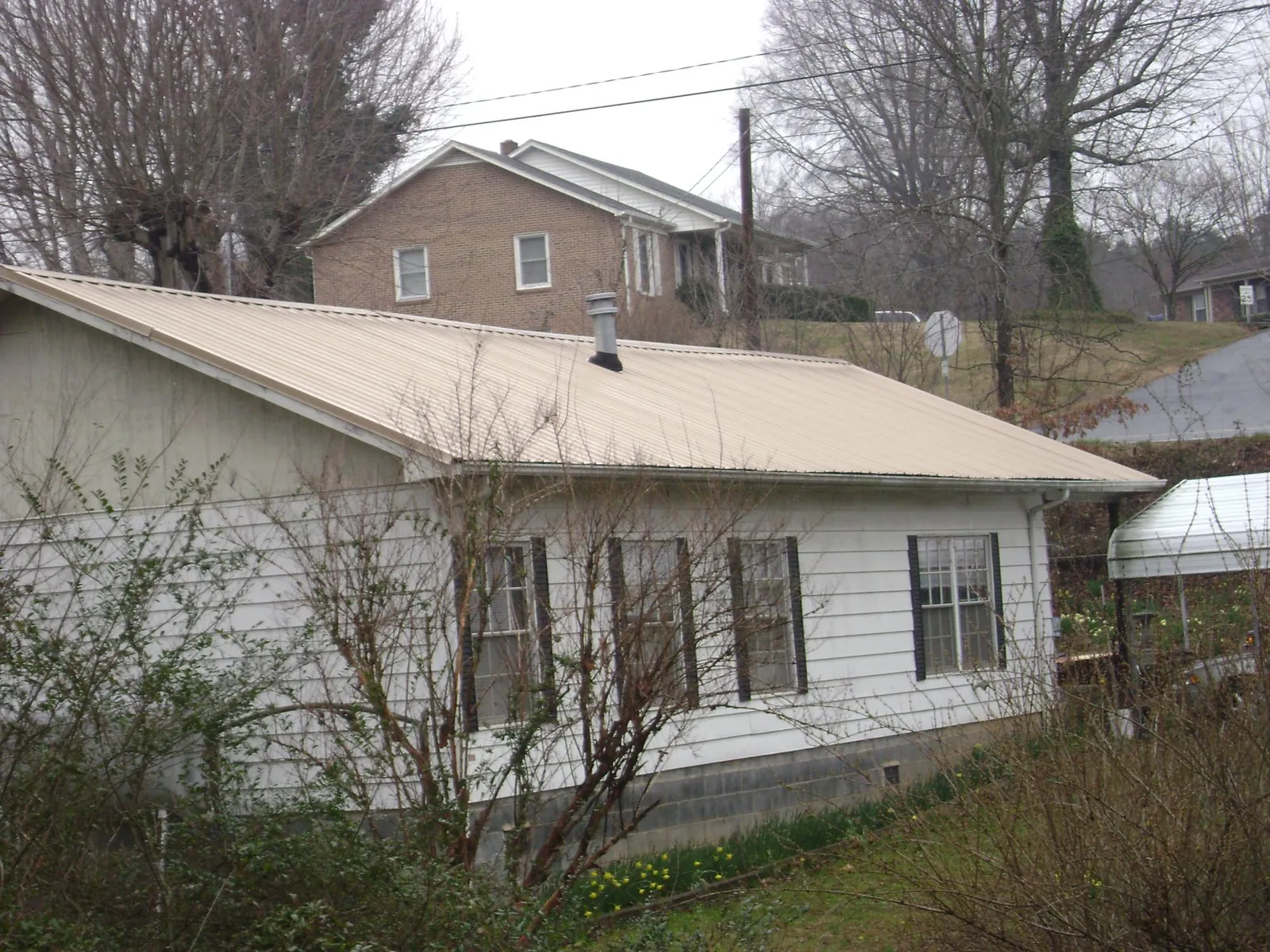 Tan metal roof on a white sided house set into a hillside — Commercial Roofing by Roofing Brothers in Arendtsville